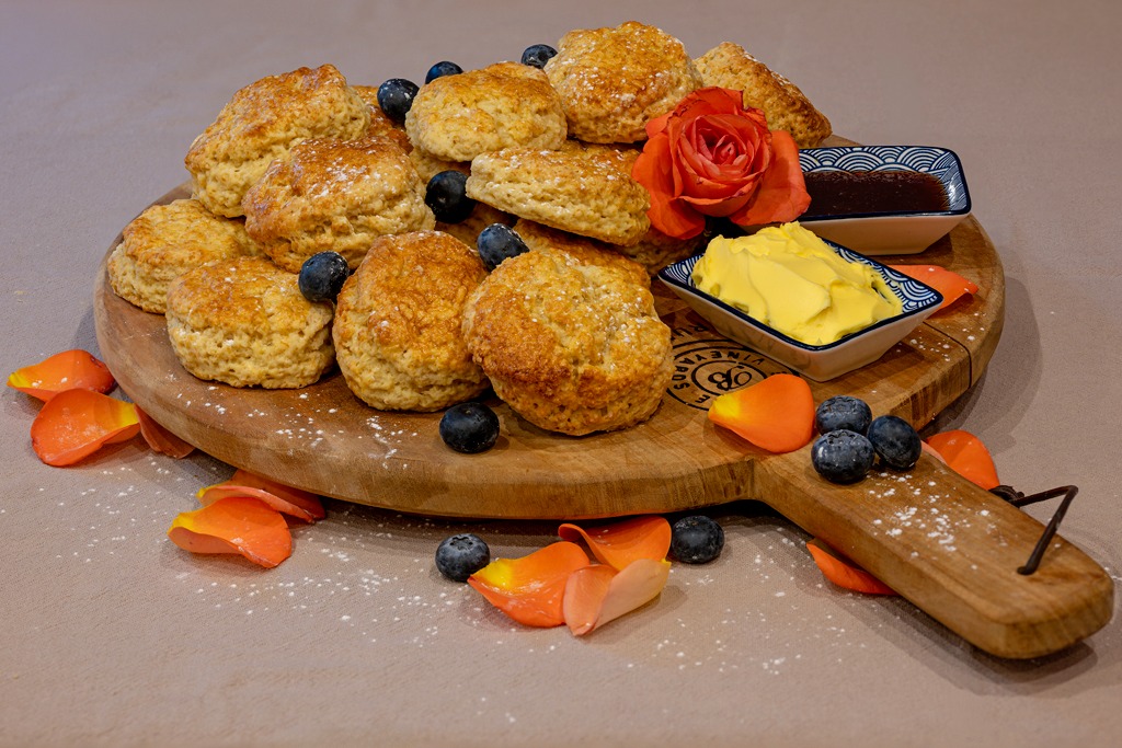 Warm scones on a wooden board with butter and jam